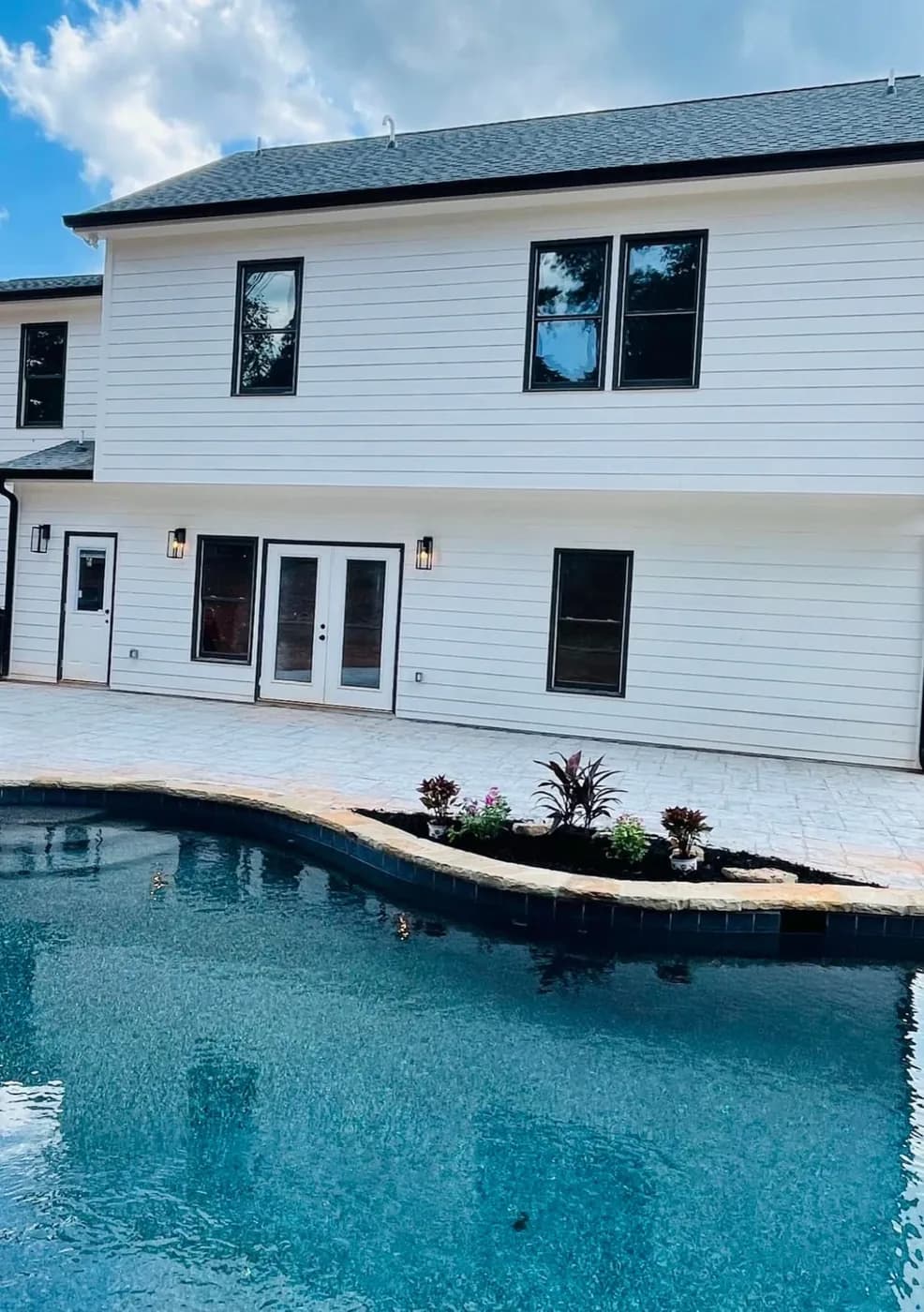 White modern farmhouse with black window frames behind a rectangular pool